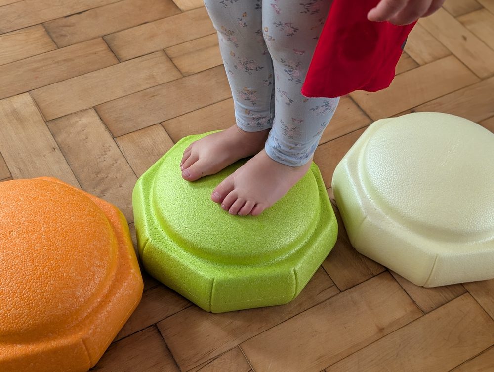 A child balancing barefoot across wobble stepping-stones, a close-up of their feet