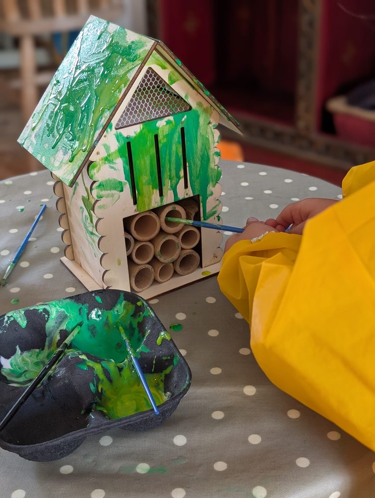 A child's hand painting a wooden bug hotel green